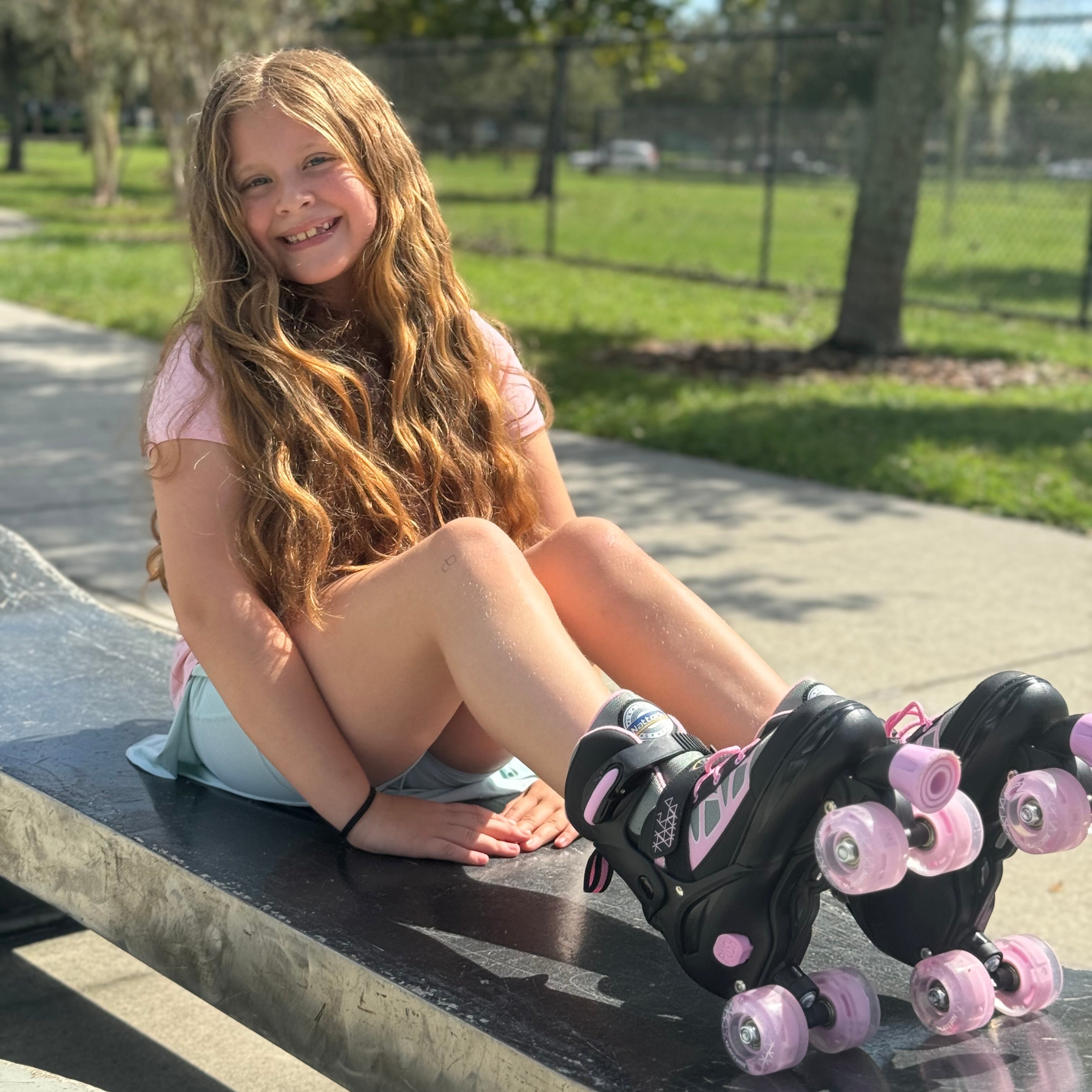 Young girl with long hair sitting on a bench wearing roller skates with pink wheels.